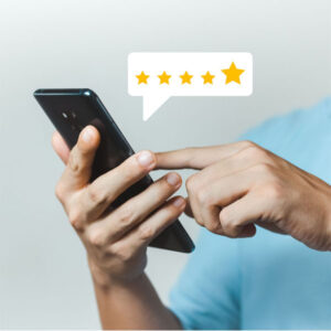 A person in a light blue shirt is using a smartphone. An illustrated speech bubble above the phone displays five yellow stars, indicating a positive rating or review. The background is plain light grey.