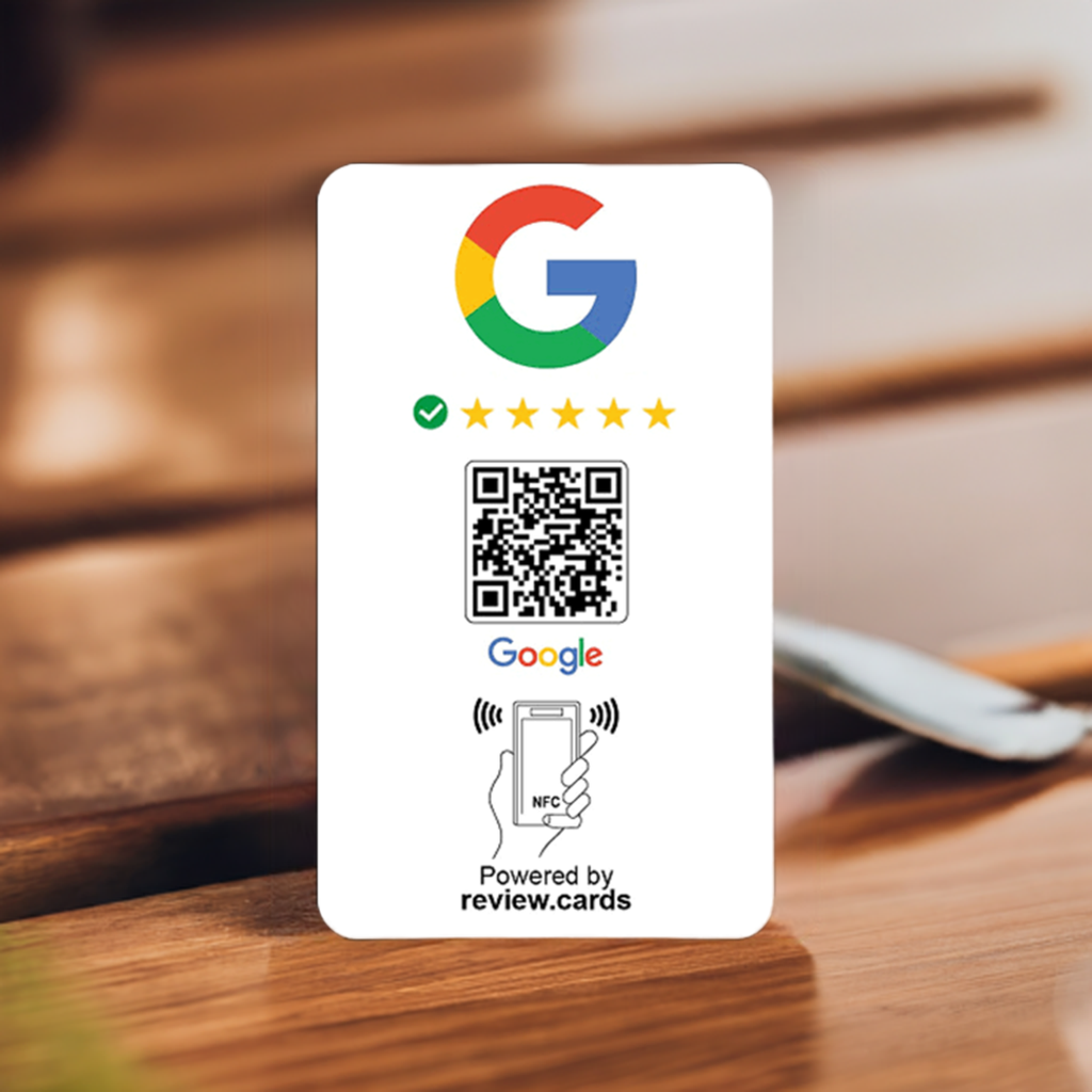 A Google Smart Review Card Multi Packs - Free Delivery is shown with the Google logo and five gold stars beneath it. Below the stars is a QR code followed by the Google logo. At the bottom, there's an icon of a hand holding a phone with the text “NFC” and “Powered by review.cards.” The card is set on a wooden surface.