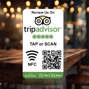 A stylish table sign in a restaurant promoting reviews on TripAdvisor features the logo, a QR code, and a Wi-Fi symbol indicating NFC functionality for smart cards. The text reads "Review Us On" and "TAP or SCAN." The background showcases out-of-focus lights and chic restaurant decor. This is one of the 1 TripAdvisor Tap or Scan Smart Cards – includes free delivery.