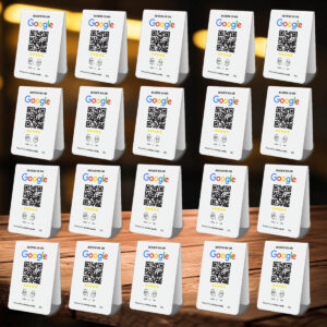 A 4x5 grid of 20 Google Tap or Scan Table Tents with QR codes and the Google logo. Each card has the text "REVIEW US ON" at the top and pictures of a coffee cup and a smiling face at the bottom, standing on a wooden surface with a blurred background.