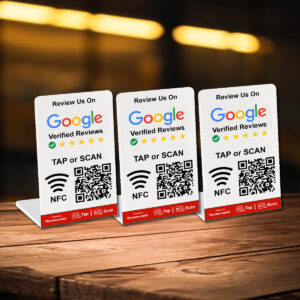 Two Google Tap or Scan Stands - FREE Delivery encourage customers to leave reviews on Google Verified Reviews. Each stand features a QR code for scanning and an NFC icon for tapping, along with the text "Review Us On Google Verified Reviews" and star icons indicating review ratings. The background is a blurred indoor setting.
