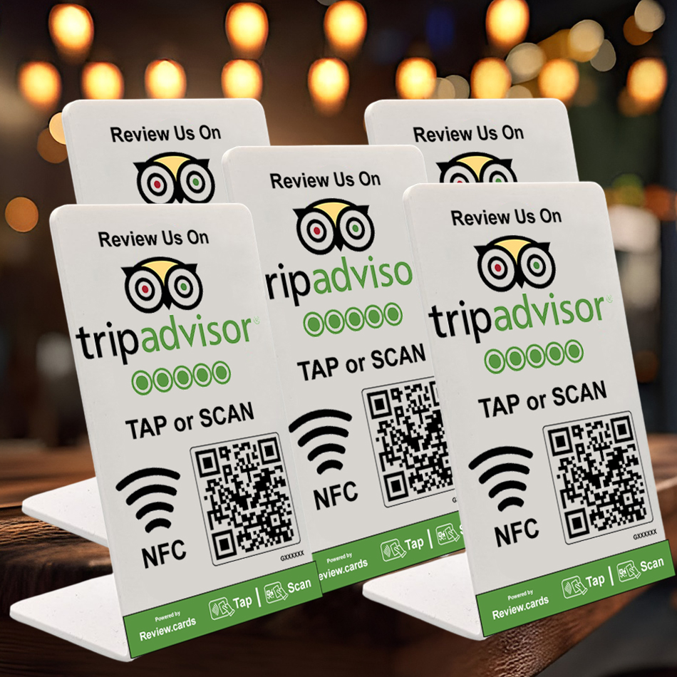 Five tabletop signs display a request for reviews on Tripadvisor. Each sign features the Tripadvisor logo, a QR code, NFC symbol, and text reading "Review Us On Tripadvisor TAP or SCAN." The background shows a blurred interior with warm lights. These 5 TripAdvisor Tap or Scan PoP Stands inc FREE Delivery are perfect for gaining quick feedback.