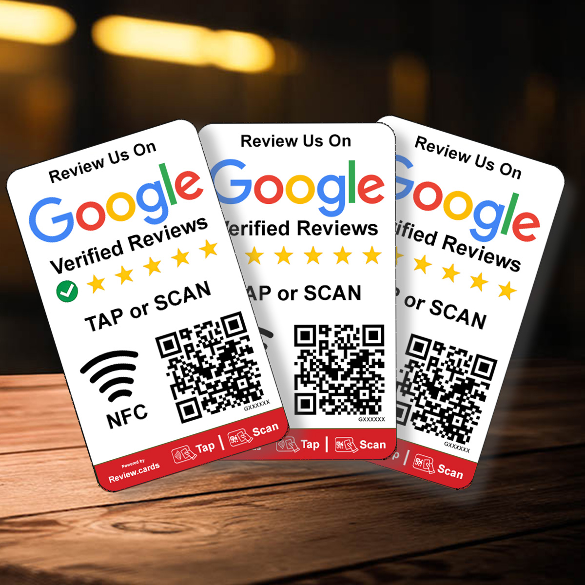 Two Google Smart Review Cards on a wooden surface display "Review Us On Google Verified Reviews" with QR codes and instructions to tap or scan using NFC. Each card shows Google's logo, star ratings, and icons for NFC and QR scanning. Background is blurred with warm lighting.